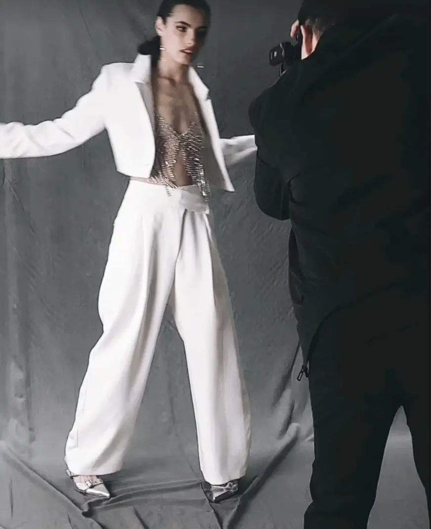Joel, vestido de negro, fotografía a una modelo con traje blanco frente a un fondo gris